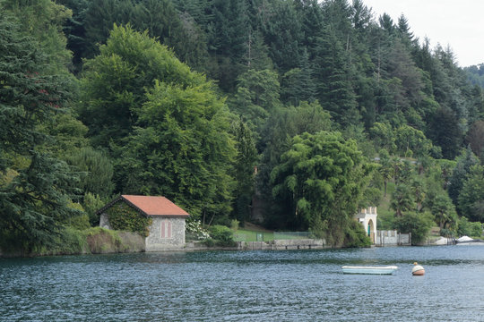 A house with trees next to the lake Orta shore in Novara province, northern Italy, with a boat