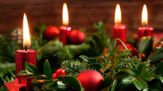 Decorative advent wreath of green fir twigs and mistletoes with red candlelight and shiny baubles and stars in front of a rustic wooden wall, close-up studio shot with selective focus, nobody