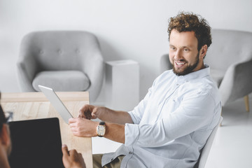 portrait of smiling businessman using tablet while having conversation with colleague in office