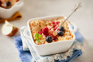 Traditional British apple crumble on portion baking dish with fresh berries