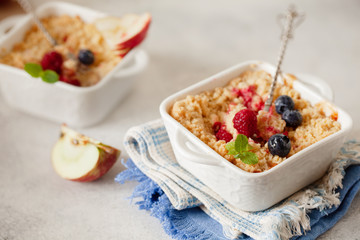 Traditional British apple crumble on portion baking dish with fresh berries