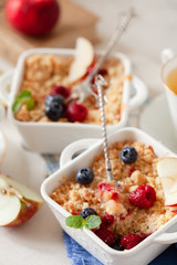 Traditional British apple crumble on portion baking dish with fresh berries