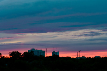 the end of a summer day: colorful sunset over line the outskirts of the city, dark sky with clouds, silhouettes of chimneys, cranes, towers and houses