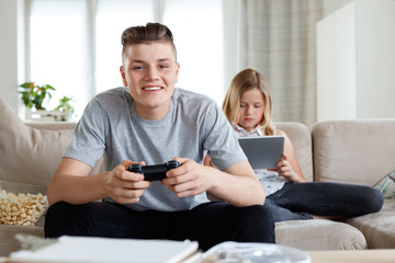 Siblings at home, boy playing video game, girl watching tablet