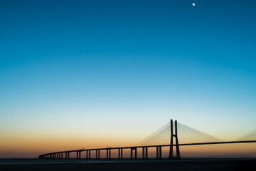 Fototapeta na wymiar Vasco da Gama's Bridge during a sunset with clear sky and the Moon