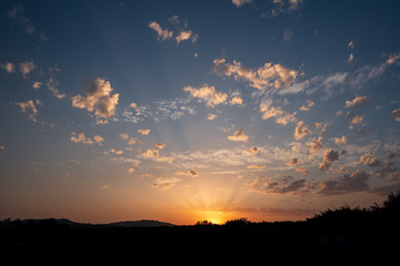 Sunset with sun almost hidden and shadows on the clouds and blue sky