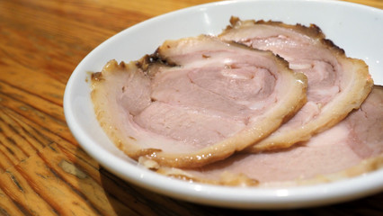 Chashu pork 3 pieces slice on the white color dish and wood table which additional menu for topping on tonkotsu ramen famous traditional food in Sapporo Hokkaido Japan.