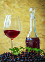Red berry wine in a glass and in decanter and ripe black currant on a table over wooden background. Homemade alcohol drink. 