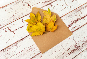 Close up of opened paper envelope on old white wooden background with yellow leaf. Vintage style of communication. Romantic gesture in golden autumn season.