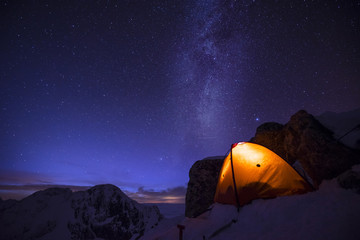 Orange tent under starry sky and milky way. Extreme and adventure winter camping under the stars in winter alpine like landscape. Epic bivi spot. Mountaineering and alpinism tent shining in the night. © Ondra
