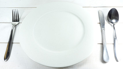 White plate with spoon, knife and fork a white wooden table background, Top view with copy space..