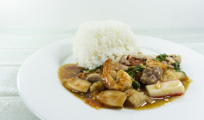 Thai food, Fried Basil seafood in a white plate on wood floor table,fork and spoon,Front view Copy Space.