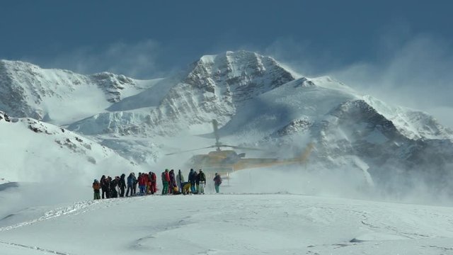 Mountain Helicopter Taking Off. Helicopter on the top of the mountain Takes off from ground. Heli Skiing Helicopter. Group of skiers waiting for helicopter. Slow Motion. Skiers and snowboarders