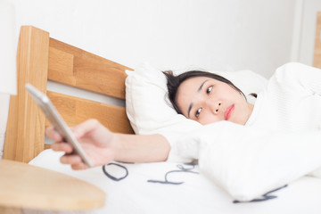 Naklejka premium Beautiful Attractive Asian young woman wake up in the morning and looking in smartphone to turn off alarm clock