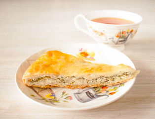 Oriental pastry fresh hot traditional Ossetian pie with homemade cheese, spinach and herbs cut into pieces in saucer with cup of tea. Close-up, selective focus.