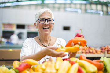 Good-looking senior woman wearing glasses buys pepper on market