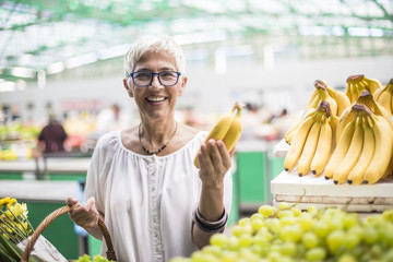 Good-looking senior woman buys bananas at the market