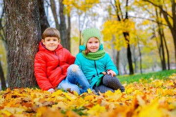 Naklejka na ściany i meble little guy with a girl sitting near a tree on the autumn foliage