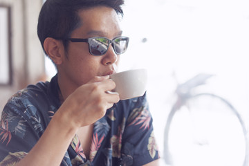 A hipster boy with sunglasses is drinking hot coffee.