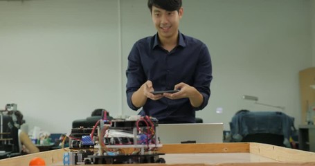 Electronics engineer programming and control robots to playing soccer with mobile phone in the workshop. People with technology or innovation concept. - Powered by Adobe