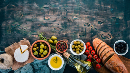 A set of olives, olive oil, bread, cheese and spices. On a black wooden background. Free space for...