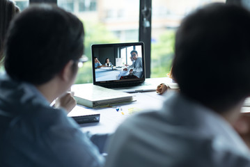 Group of Business team attending video conference discussion sitting desk in office monitor with another Business group