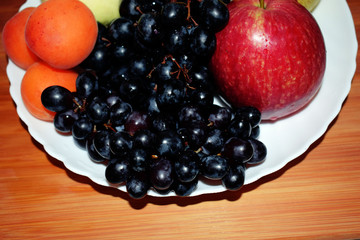 Still life of fresh fruit grapes, apples, apricots and pears on a white plate. Decorative wooden background. Ripe juicy sweet fruits. Vegetarian diet food.