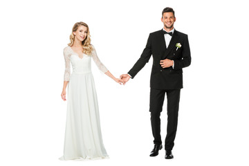 happy young bride and groom holding hands and looking at camera isolated on white