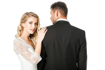 beautiful young bride leaning on shoulder of groom and looking at camera isolated on white