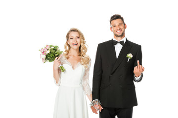 happy young bride and groom holding hands and showing middle fingers at camera isolated on white