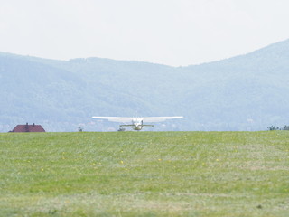 Fototapeta premium View of sport white airplane lands on green grassy airfield landscape in european Bielsko-Biala city at Poland