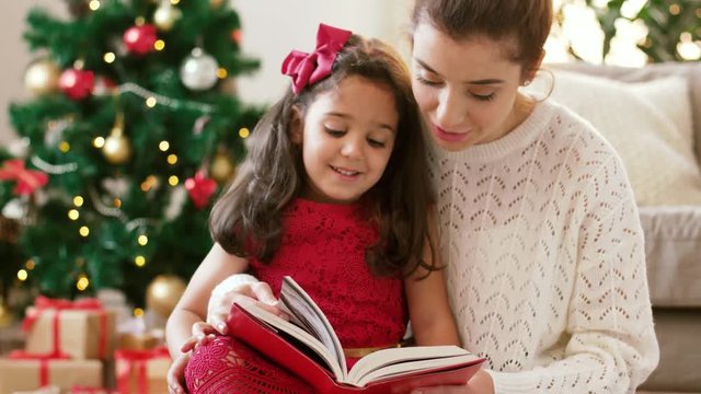 christmas, holidays and family concept - happy mother and daughter reading book at home
