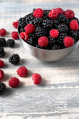 fresh organic blackberries and raspberries in a metal bowl on a wooden table, concept of diet, vitamins and antioxidants. selective focus and copy space