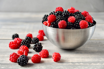 fresh organic blackberries and raspberries in a metal bowl on a wooden table, concept of diet, vitamins and antioxidants. selective focus and copy space
