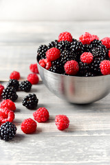 fresh organic blackberries and raspberries in a metal bowl on a wooden table, concept of diet, vitamins and antioxidants. selective focus and copy space