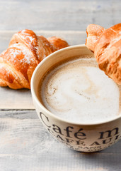  Breakfast is a large beige Cup of coffee with milk and croissants on a wooden table. on the Cup inscription in French (top down: mocha coffee, coffee with milk, coffee without sugar)