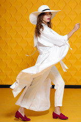 Full-length studio fashion portrait of young beautiful model wearing long white trench coat,...
