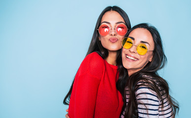 Friends forever. Two cute lovely girl friends in sunglasses posing with smile on blue background - obrazy, fototapety, plakaty