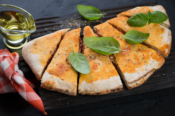 Close-up of sliced calzone pizza with fresh green basil and olive oil on a black wooden serving board, studio shot