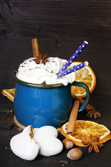 Christmas coffee cup with whipped cream, cinnamon, cocoa powder, anise, dried orange ang gingerbread cookies on wooden table. Dark retro style with copy space.