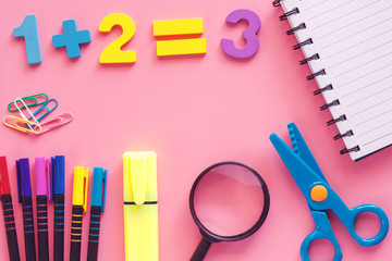 Learning supplies with notebook, scissors, magnifying glass, coloured pen, highlighter pen, binder clip and wooden number on pink background for education and back to school concept
