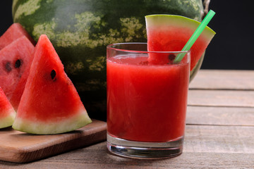 Watermelon smoothies with watermelon slices on a brown wooden table and a big watermelon in the background