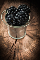Blackberries in metal bucket on vintage wooden board