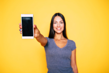 Naklejka premium Choice it! Technology, mobile, equipment for communication. Young beautiful woman shows right in camera the blank screen of smart phone on yellow background