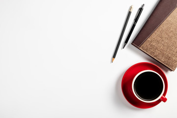 Cup of coffee with notebook on white desk, Top view, copy space
