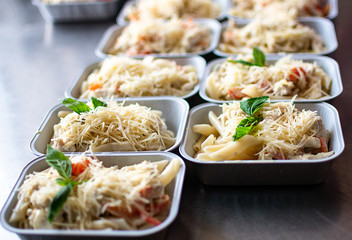 preparation of dietary dishes in the kitchen for the delivery of dietary lunch, basil, tomato cherry,  cheese, pasta and chicken fillet. concept of takeaway food. selective focus