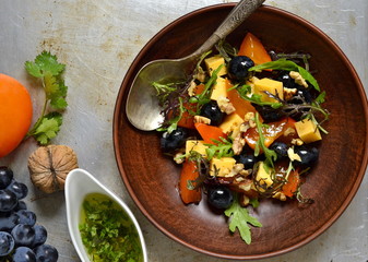 Delicious salad with persimmons, arugula, grapes and cheese, sprinkled with walnuts, top view 