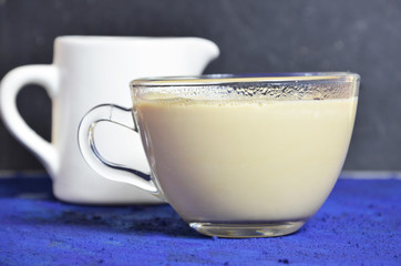 transparent glass cup with coffee and cream. milkman on the background. dark key