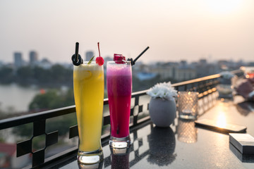 Passion fresh fruit juice with ice on outdoor table in cafe and bar. Pineapple and red dragon fruit. Urban lake on background