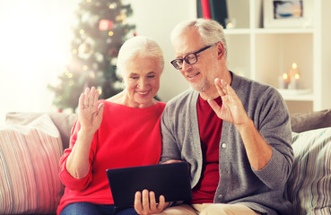 christmas, holidays, communication and people concept - happy smiling senior couple with tablet pc computer having video chat and waving hands at home